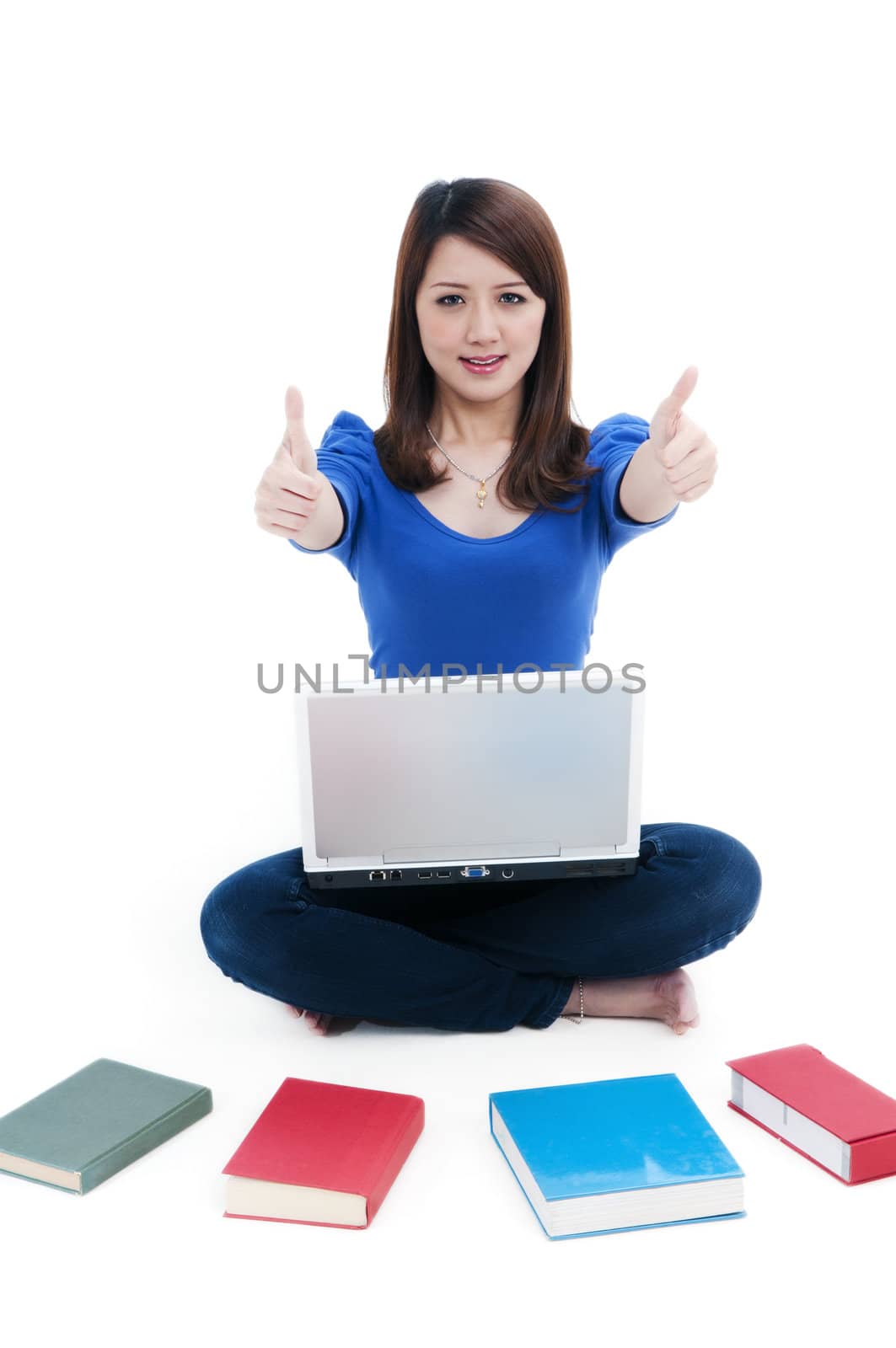 Portrait of a cute student with laptop and books spread around, giving thumbs up sign over white background.