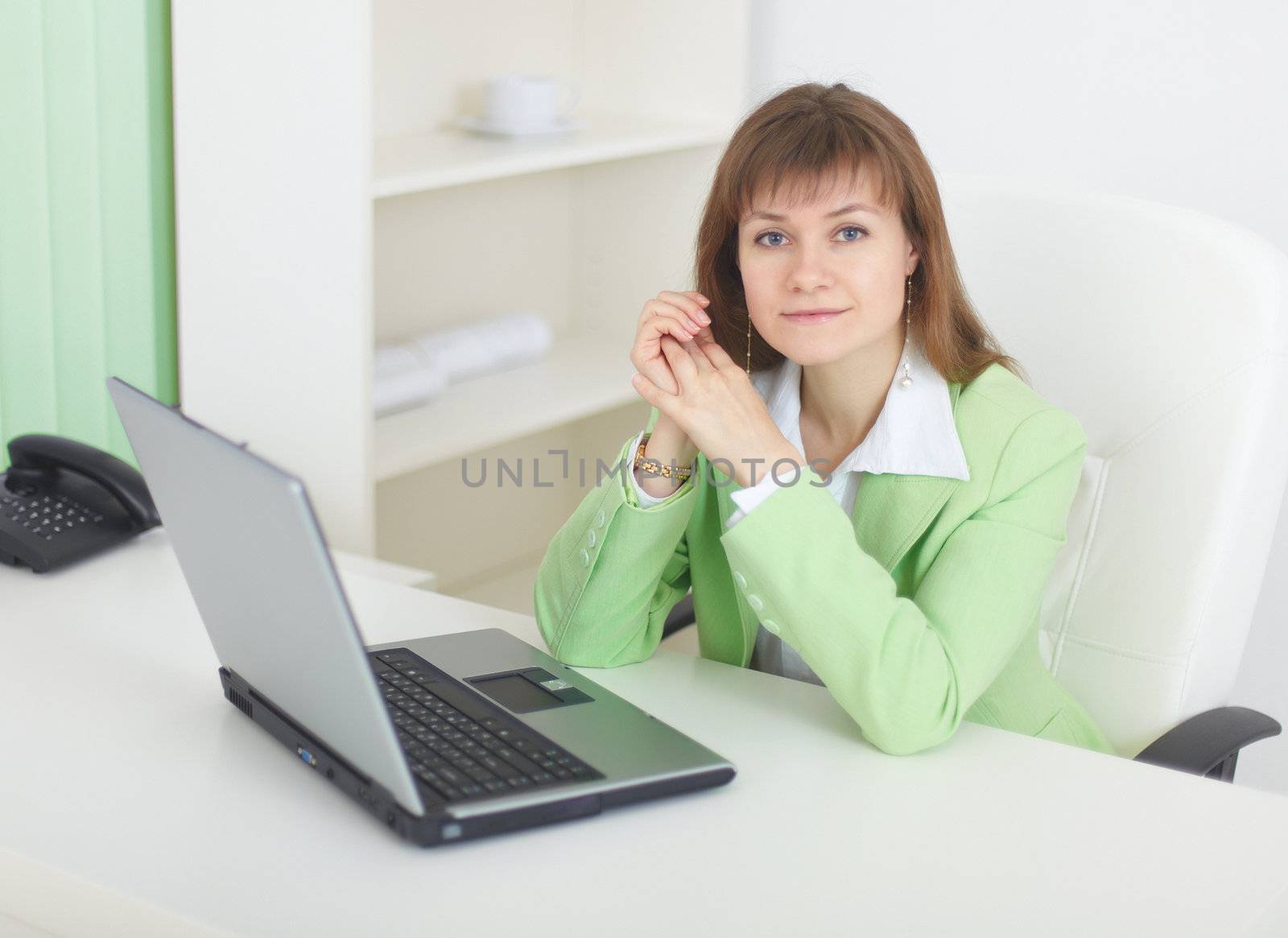 The young woman with the laptop sits at a table at light office