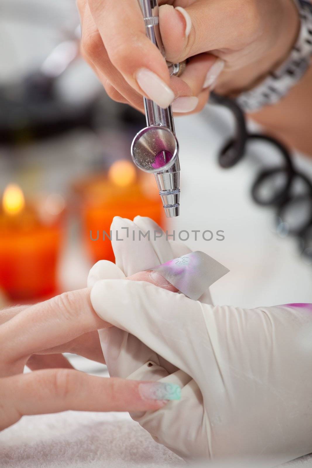 Beautician using airbrush to paint fingernails. Close-up shot