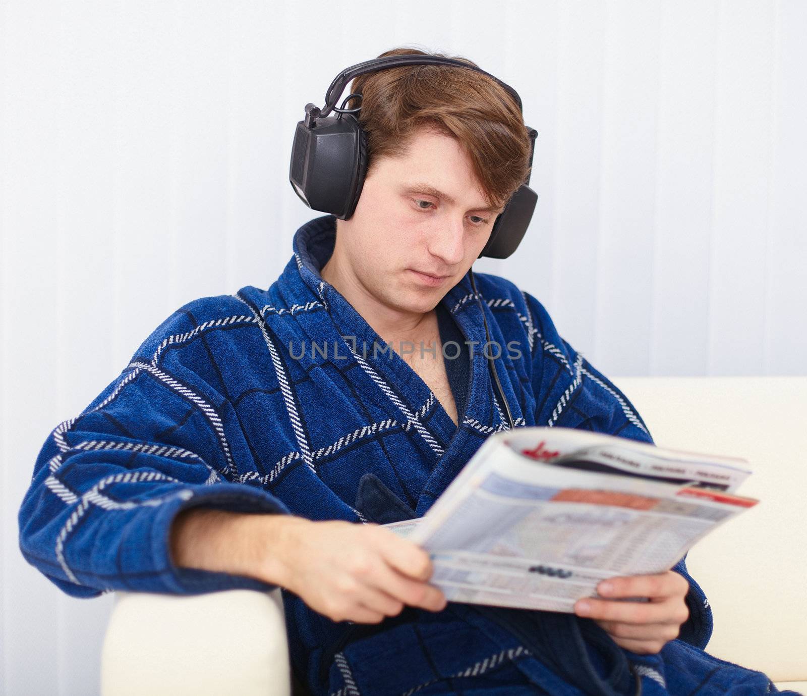 Man in big ear-phones on sofa reads newspaper by pzaxe