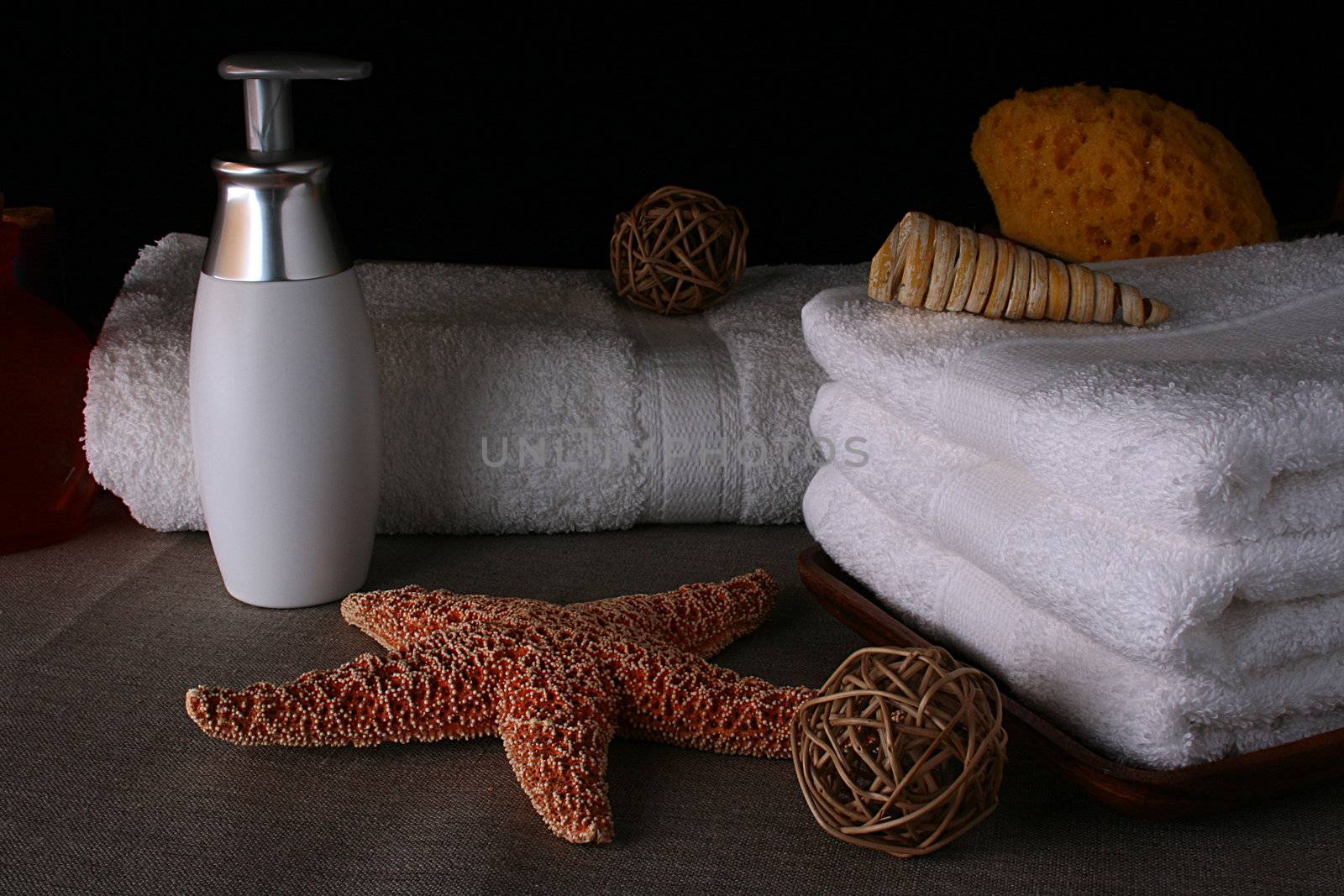 Subjects of personal hygiene: towels, liquid soap and a bast on a dense fabric with decorative elements: a starfish and an aromatic wood.