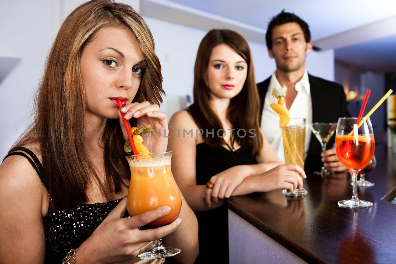 Beautiful women with friends at the bar. Drinking tequila sunrise