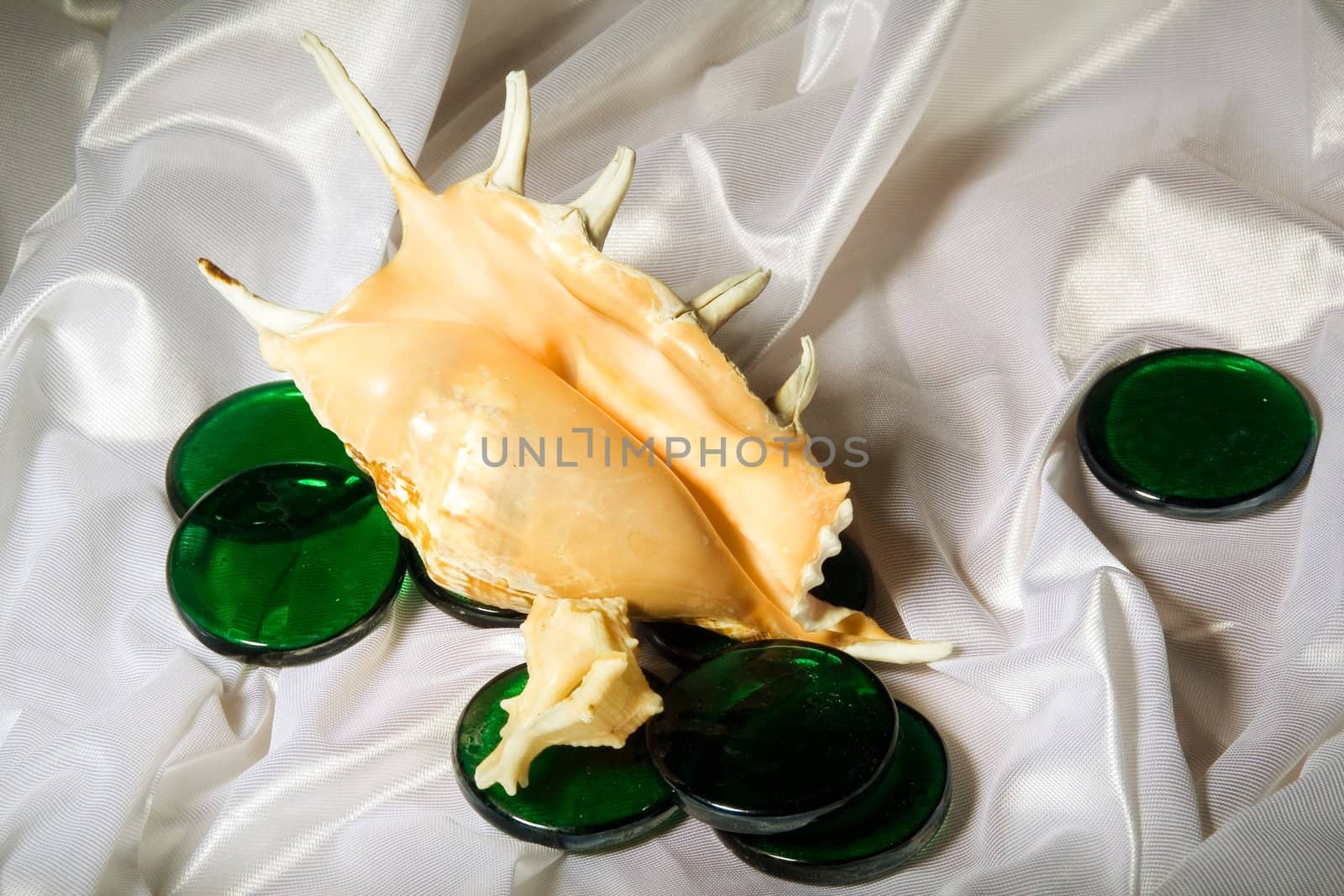 Sea shells and green decorative glass among the folds of a white textured fabric