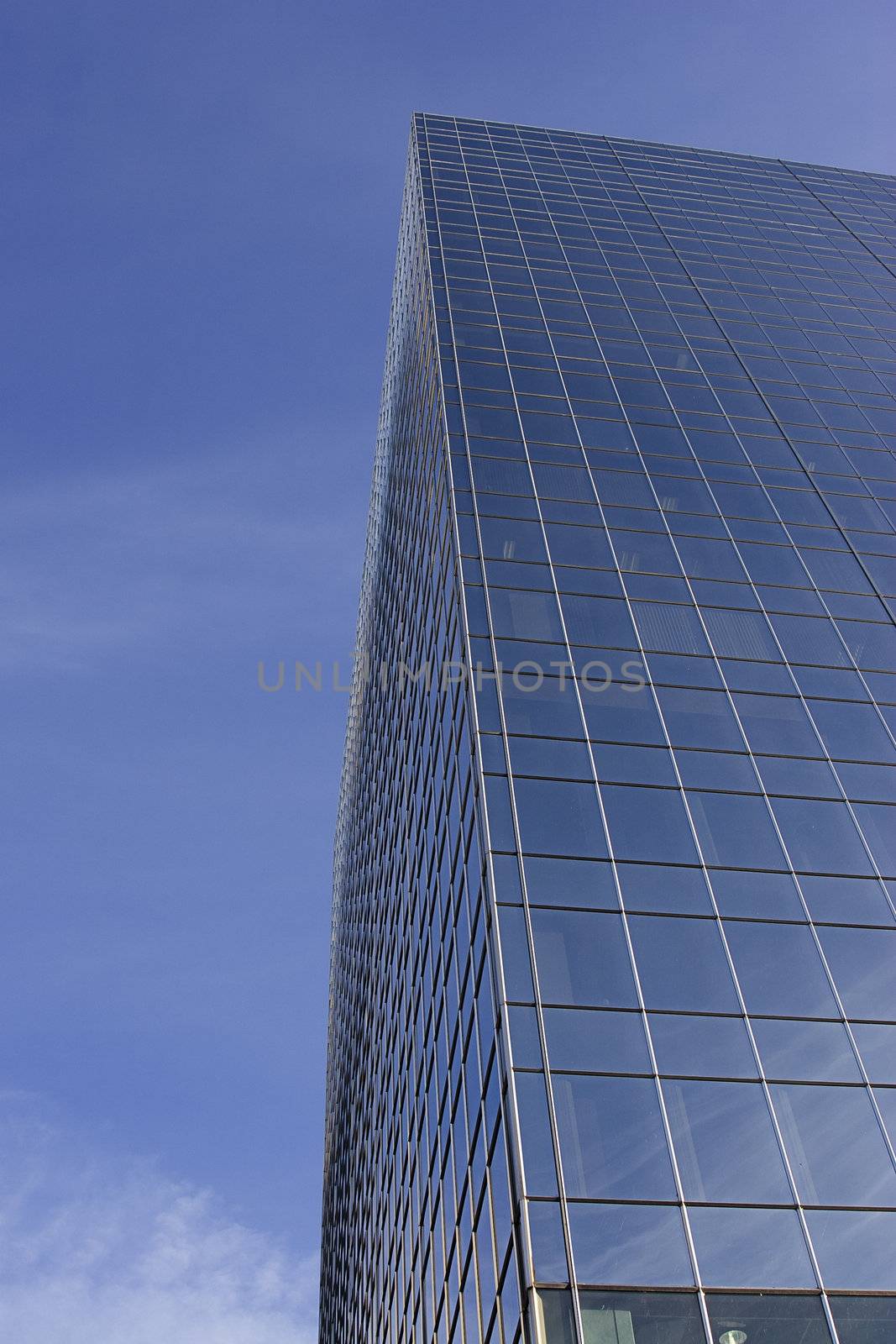 windowed skycraper building against a blu sky with thin clouds