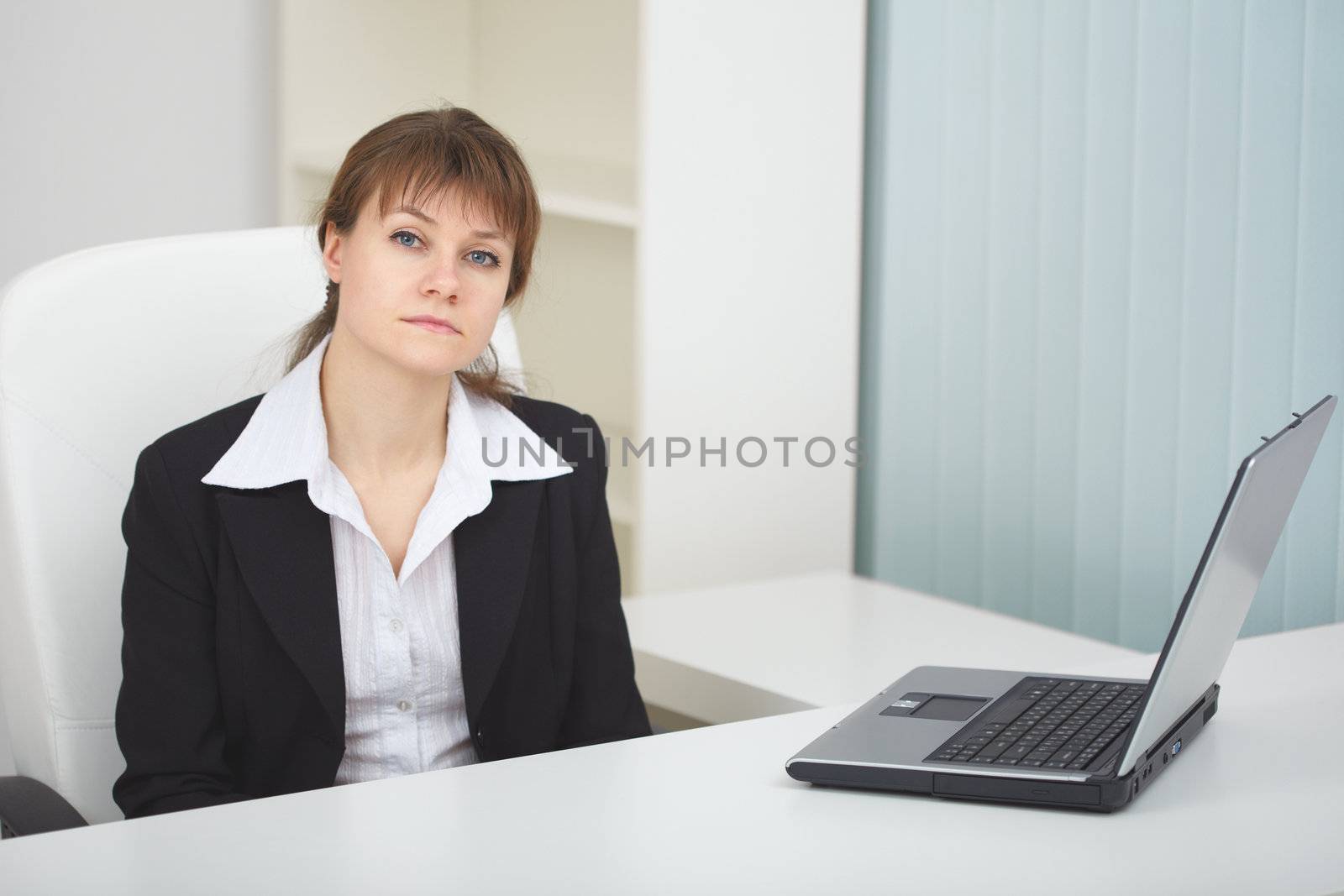 Serious woman sits at table at light office with laptop by pzaxe
