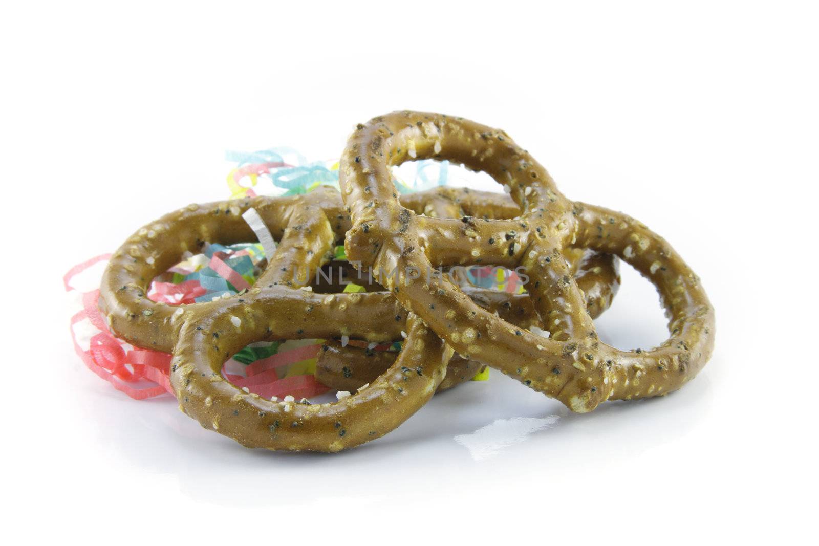 Two salty baked pretzels with party streamers on a reflective white background
