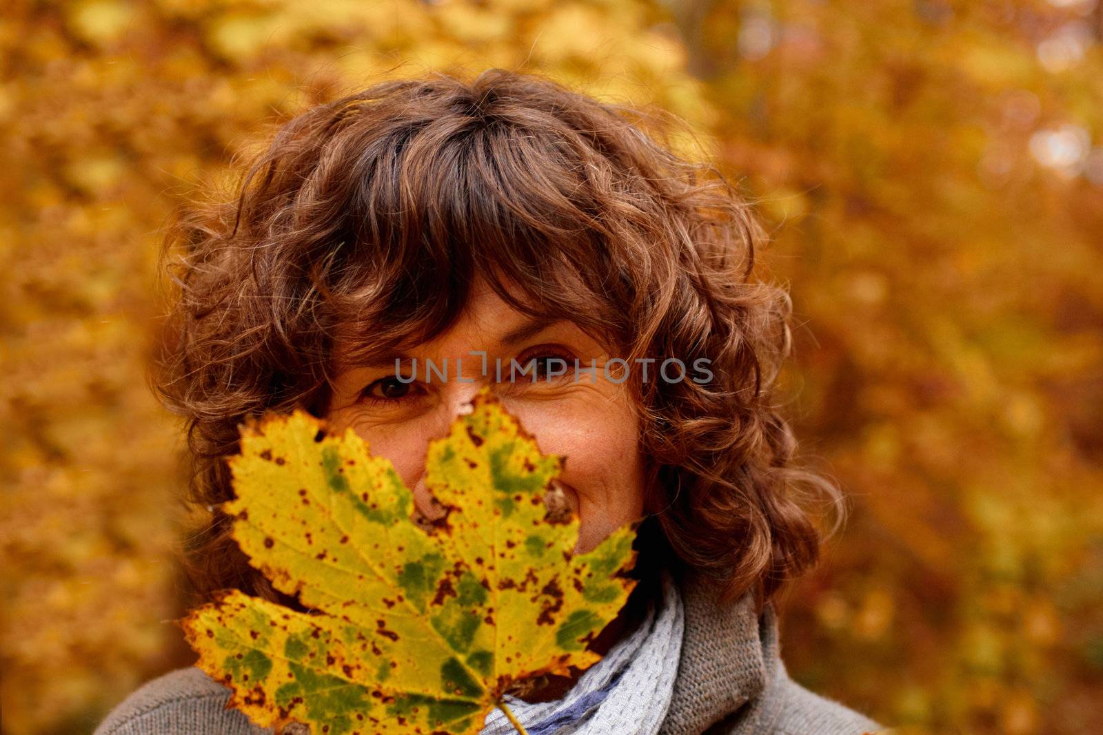 Mature woman hiding behind a  maple leaf in autumn