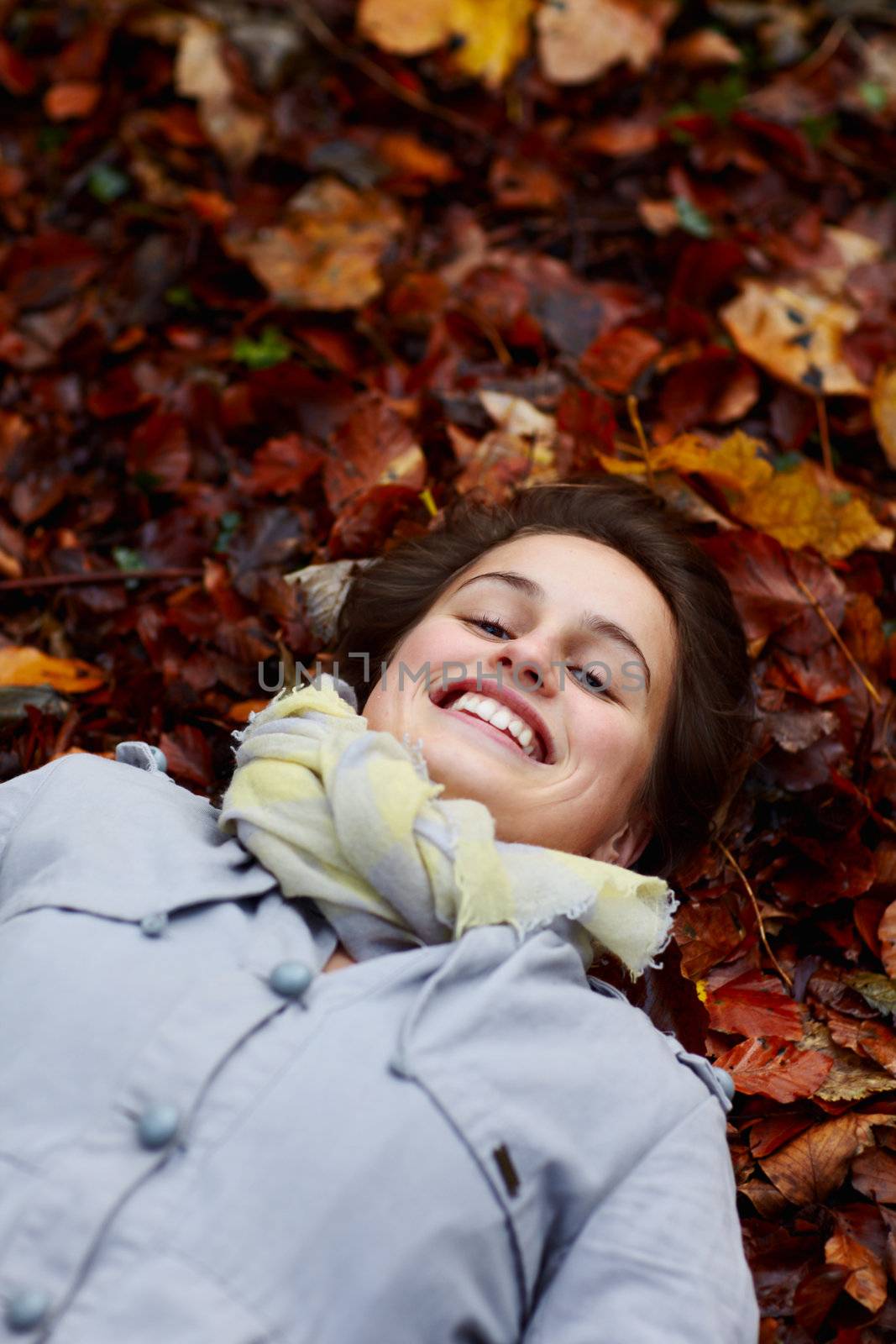 Smiling teenage girl lying in autumn leaves by FreedomImage