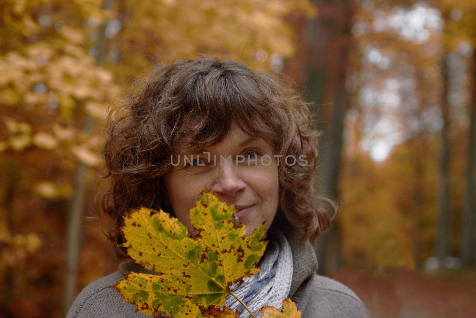 Autumn - middle aged woman looking at you from behind a maple leaf