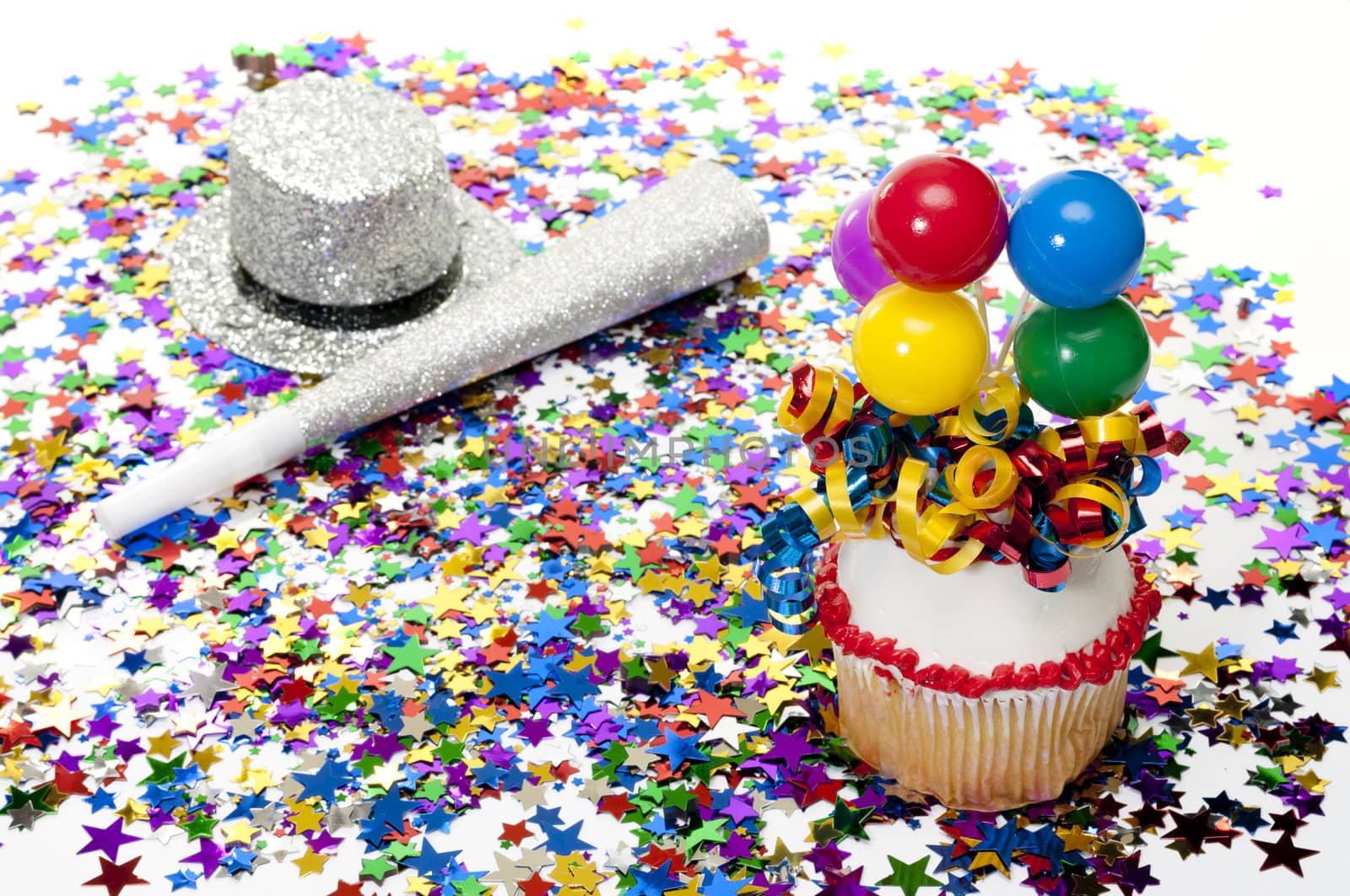 Decorated cupcake with balloons and ribbon with confetti at party. Party hat and horn in background.