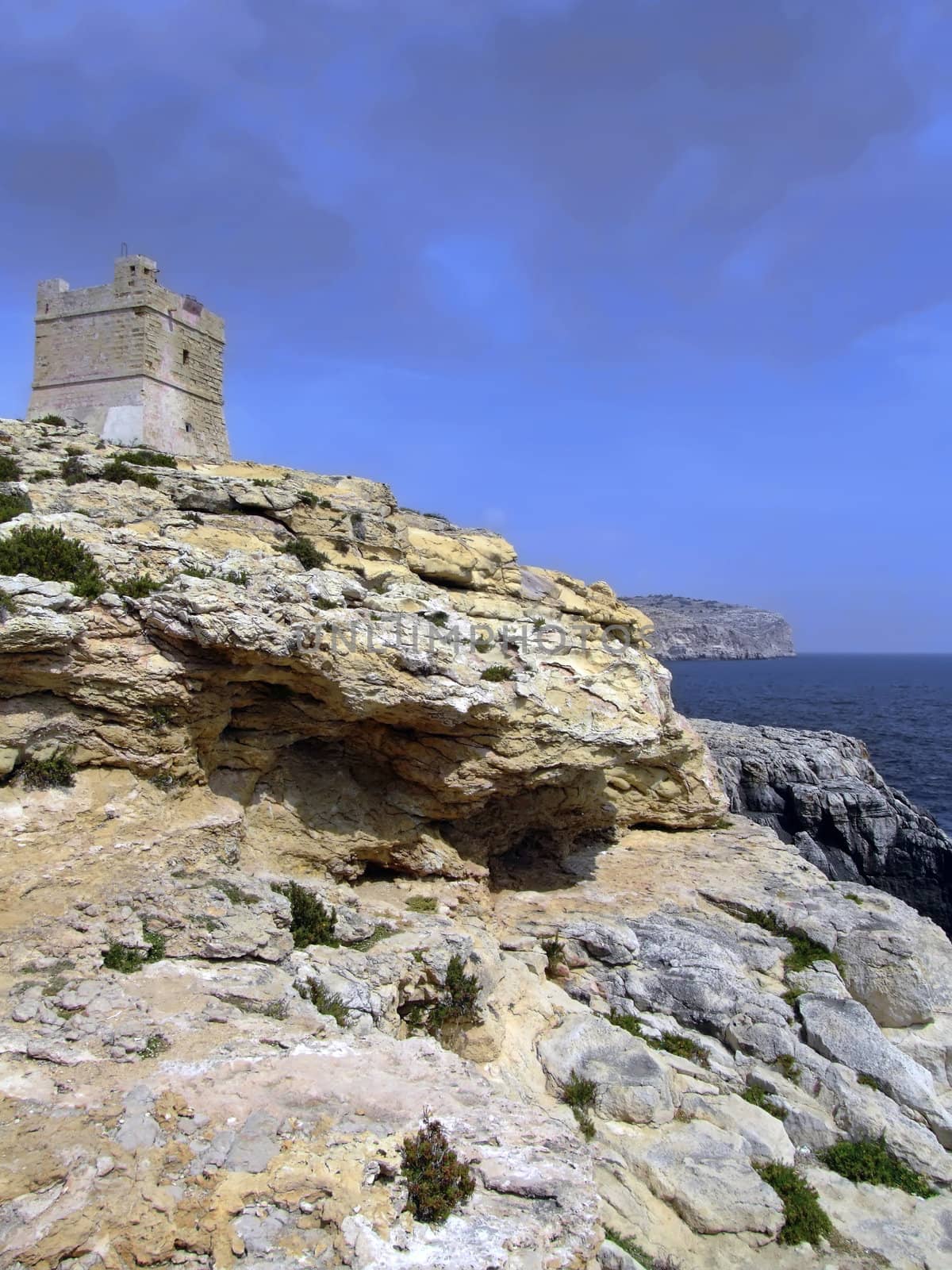 Defense tower on typical rocky coastline in Malta, punctuated with sheer drops and jagged cliffs