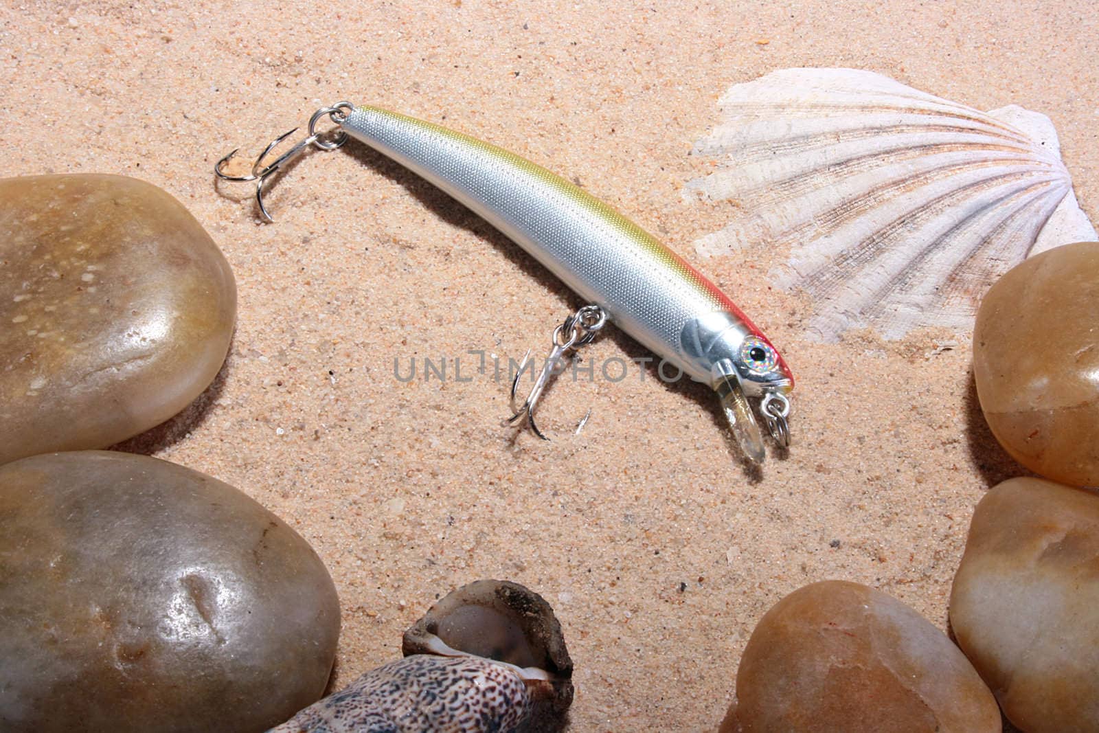 Artificial small fish - a bait for fishing in the rivers, the seas and lakes on sand with a cockleshell and pebbles.
