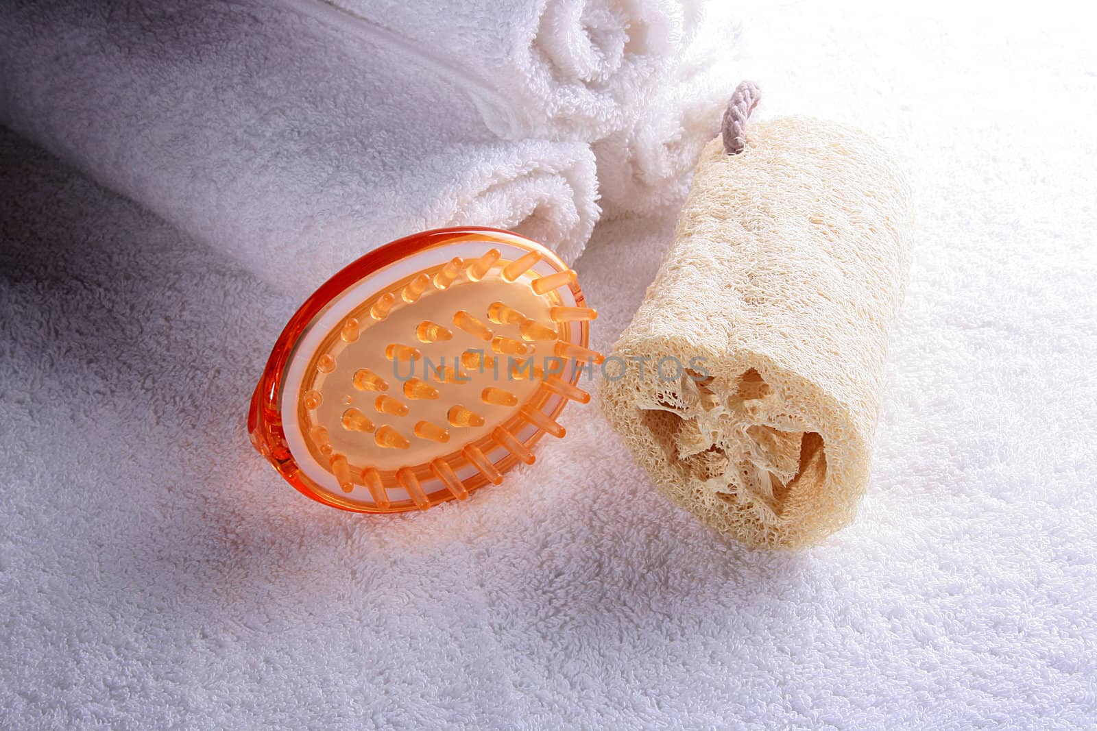 Massage brush and bast with white towels curtailed into a roll on a towel.