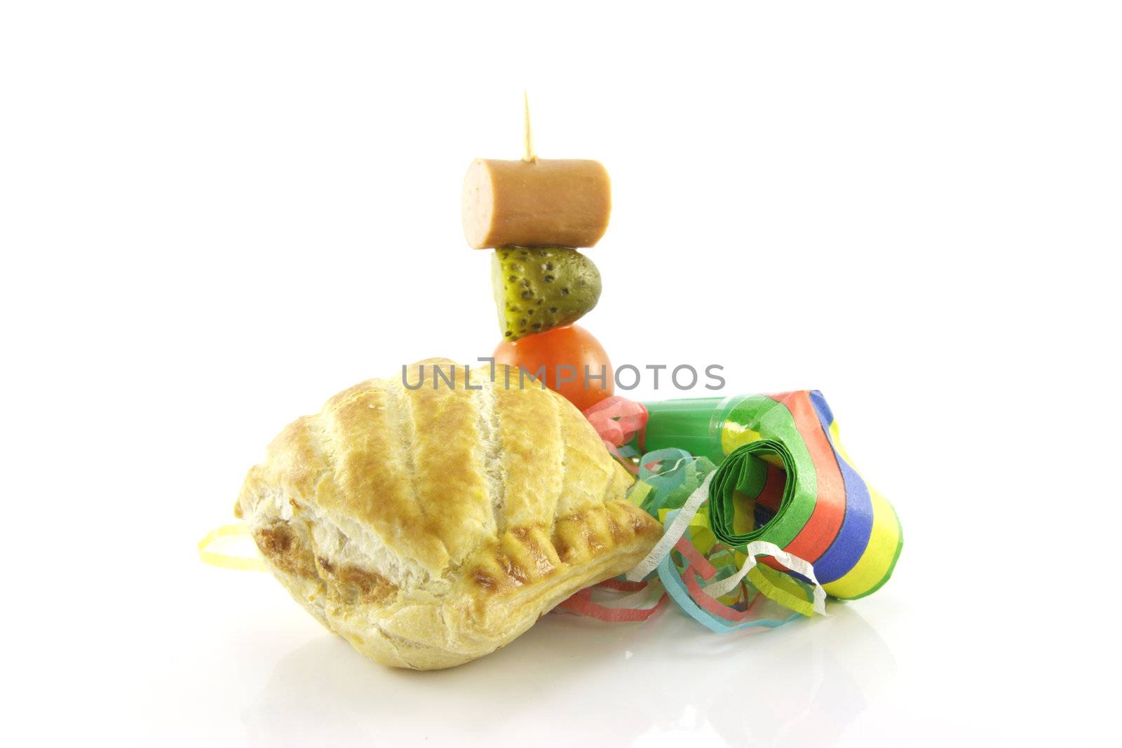 Small sausage roll with party blower and cocktail stick containing hot dog sauage, gherkin and tomato on a reflective white background