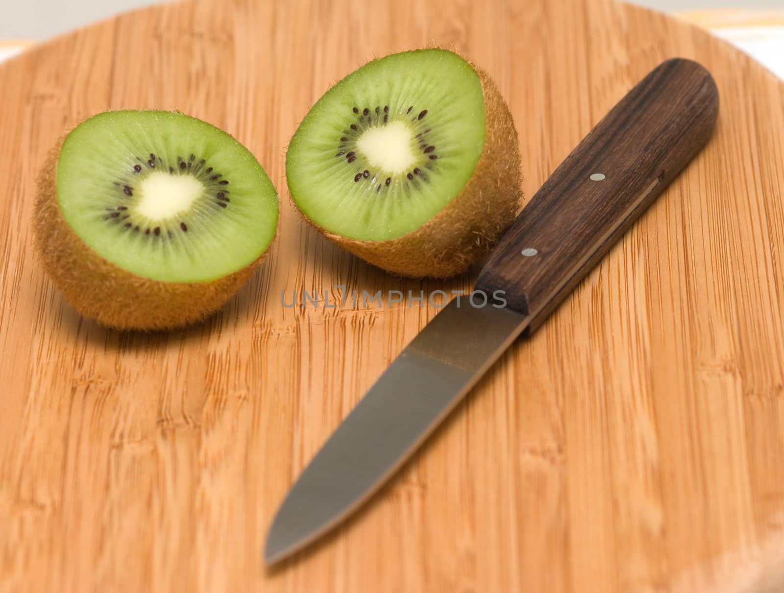 Cut half-and-half kiwi and a kitchen knife on a chopping board.