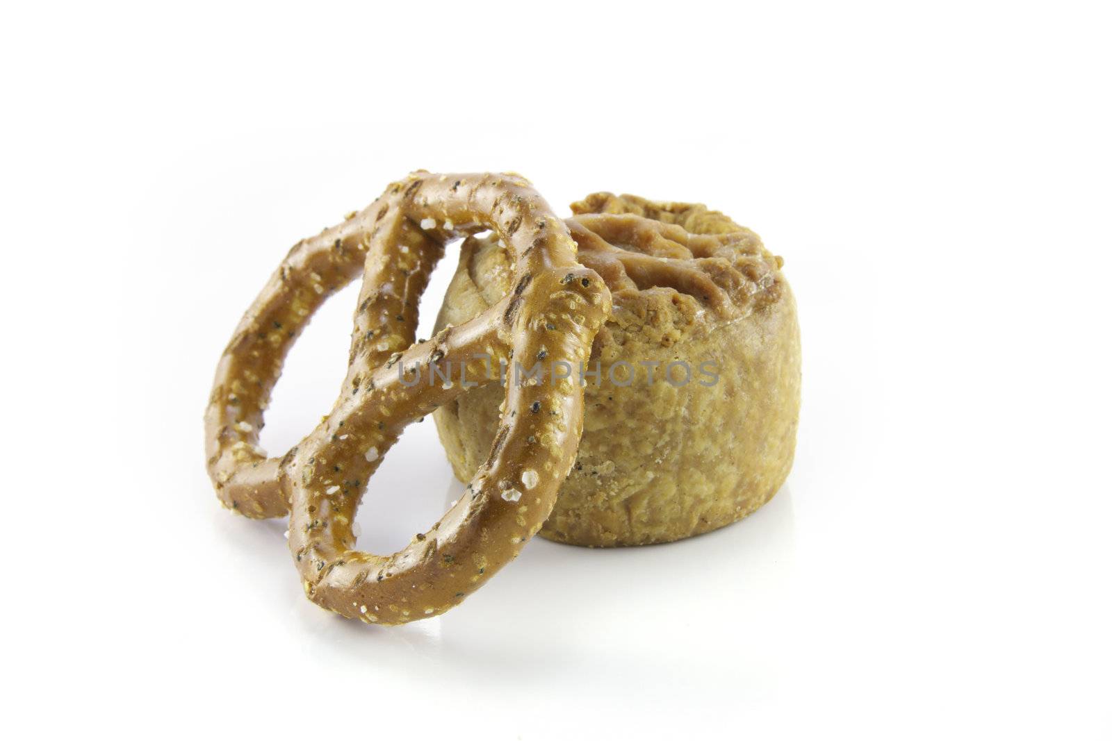 Small tasty pork pie with single salty pretzel on a reflective white background