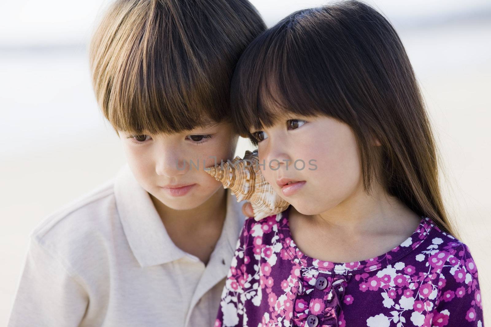 Portrait of Brother and Sister Listening To Shell at Beach