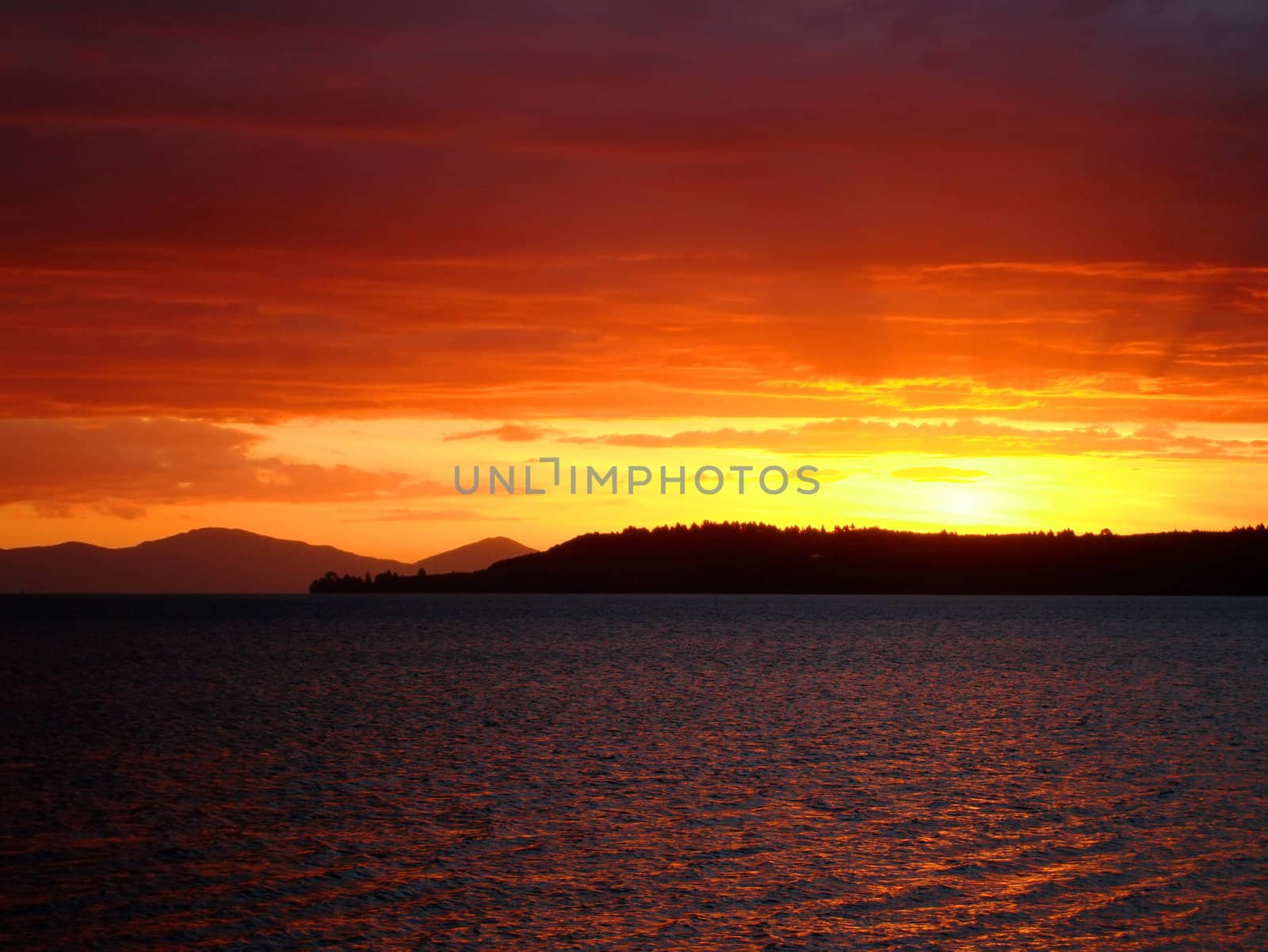 Deep red sunset over Lake Taupo (with volcanic peaks seen on the left horizon), New Zealand