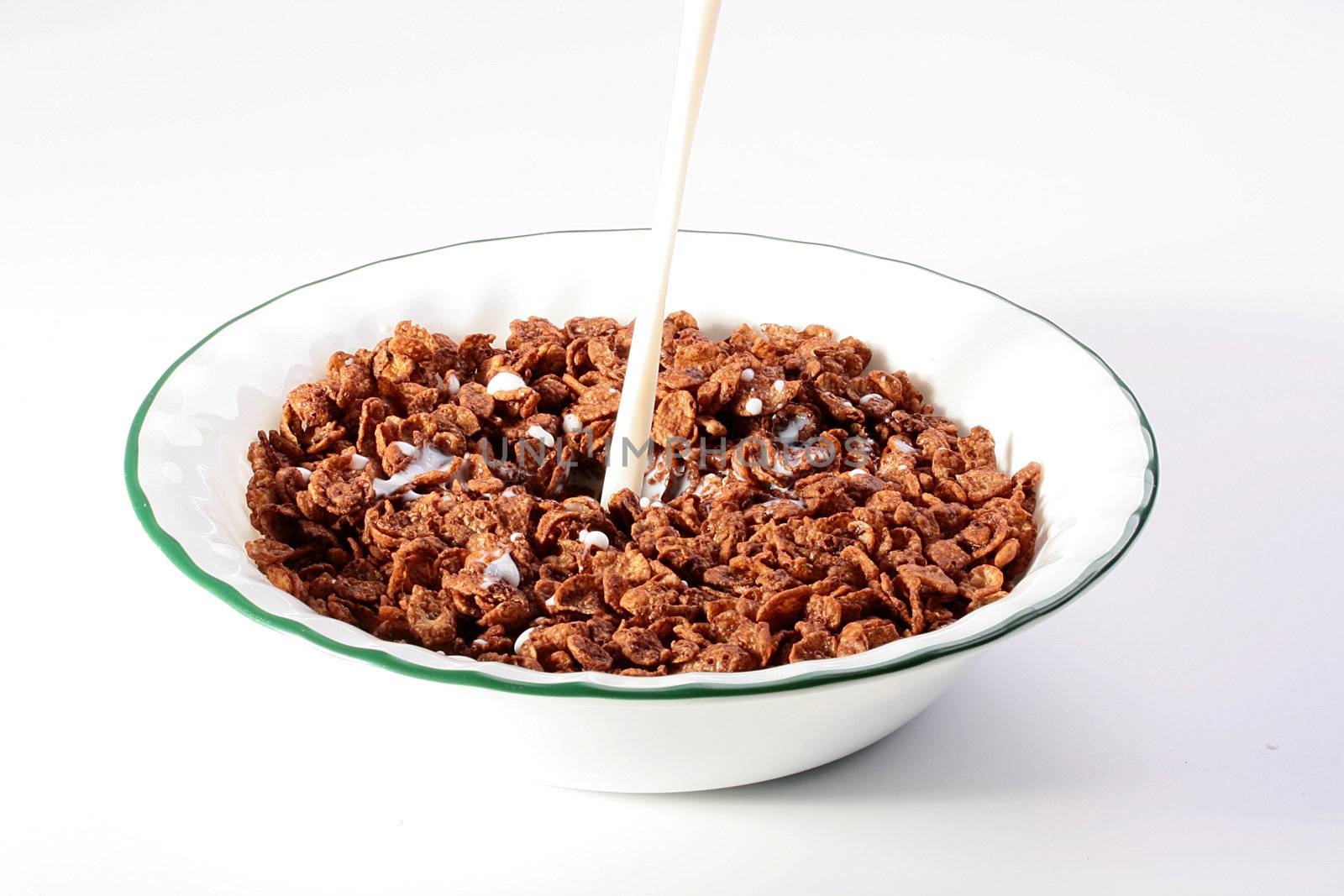 Milk pour in a deep white plate with chocolate cereals.