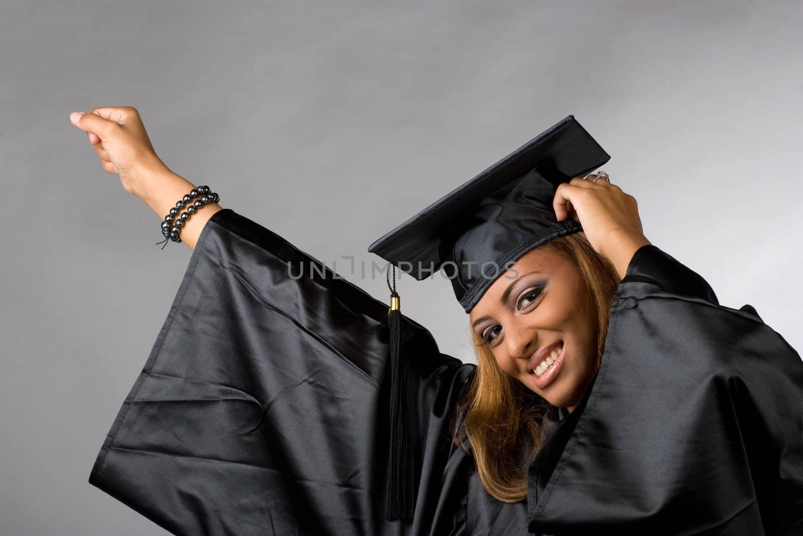 A recent graduate posing in her cap and gown isolated over a silver background.