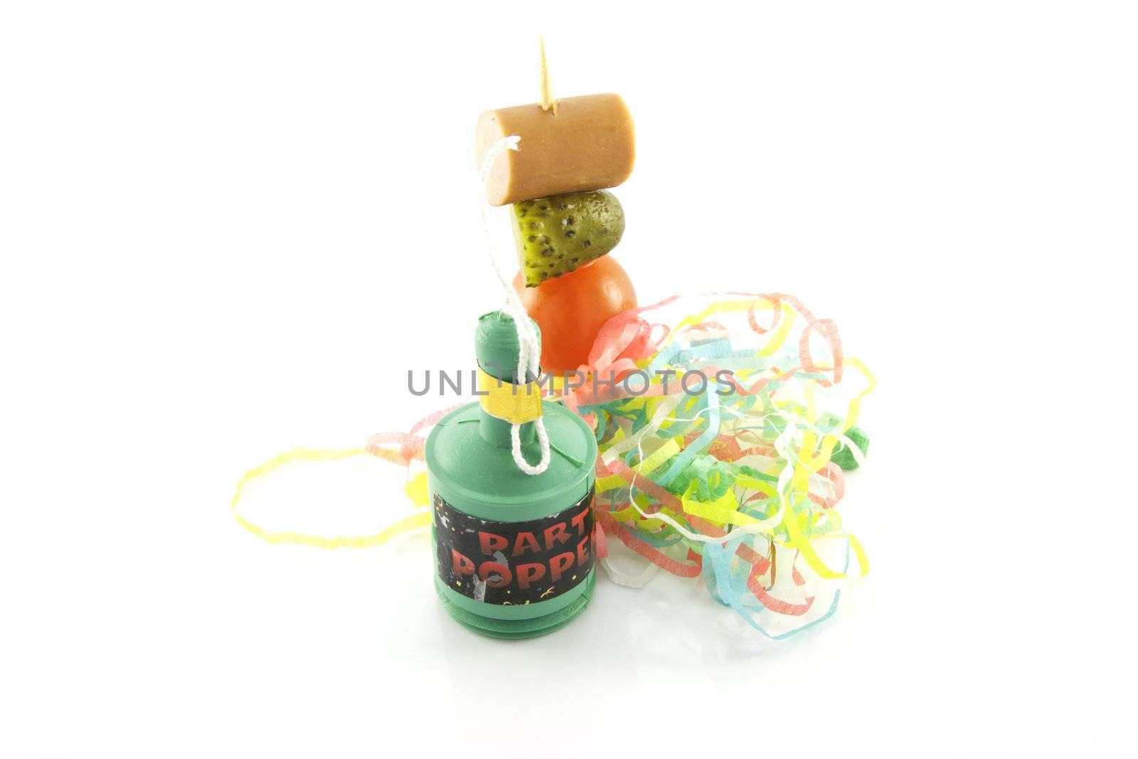 Single cocktail stick with sausage, gherkin and tomato with streamers and party popper on a reflective white background