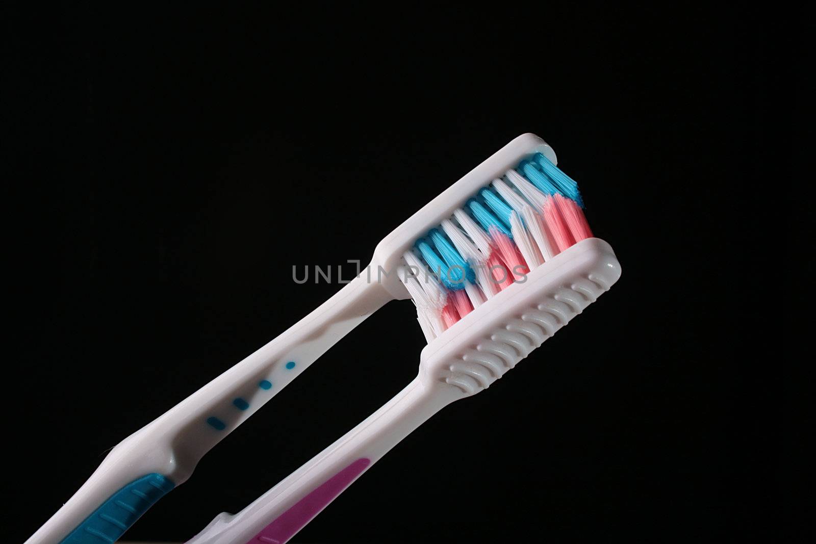 Two tooth-brushes with red and dark blue bristle on black background.