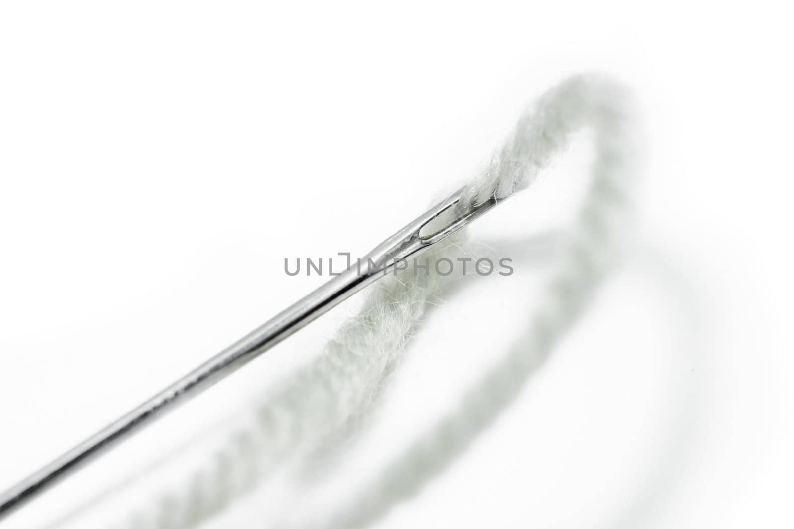 White fluffy thread is inserted into a large, sharp and shiny steel needle. Isolated on white background