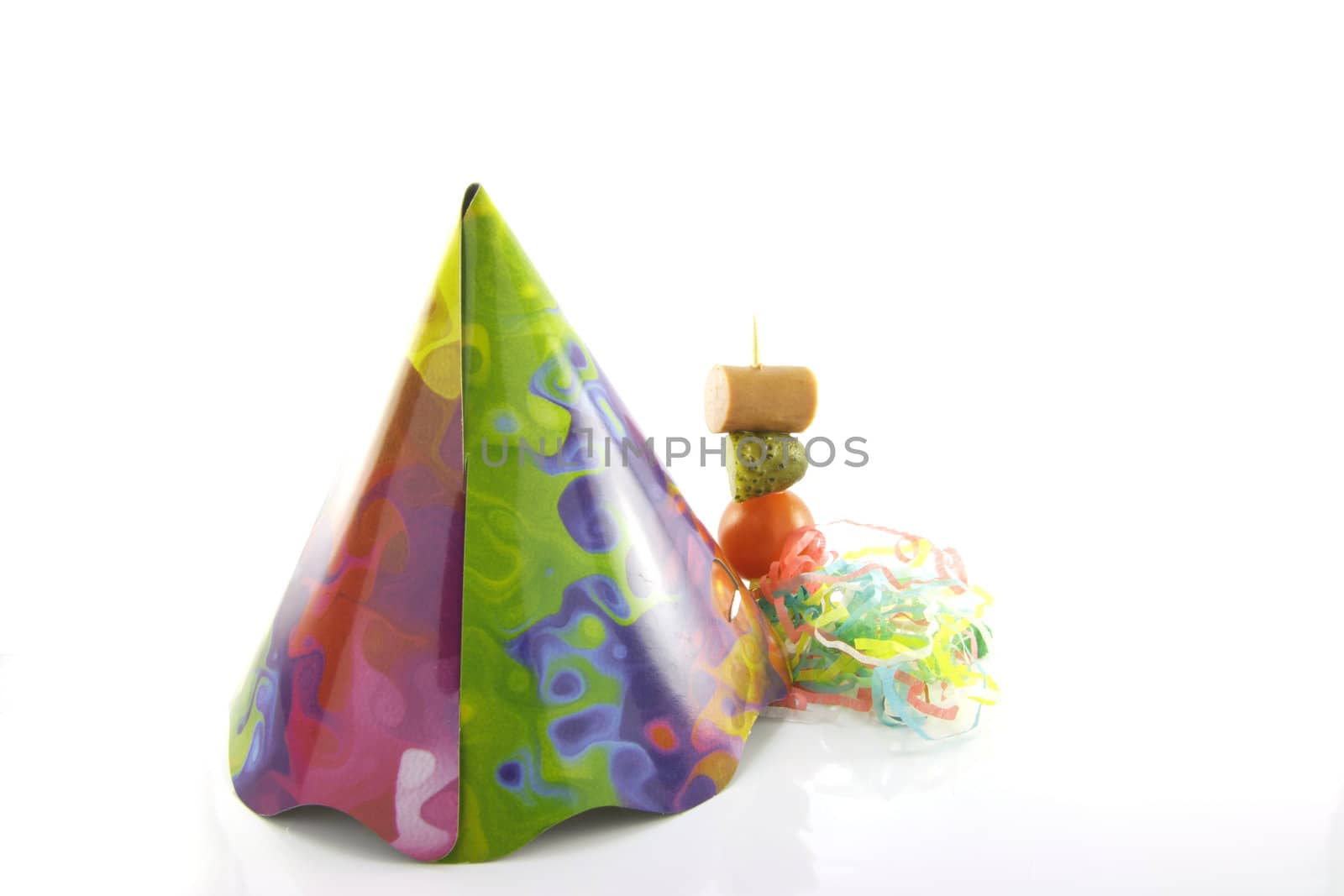 Multi coloured party hat with cocktail stick and streamers on a reflective white background