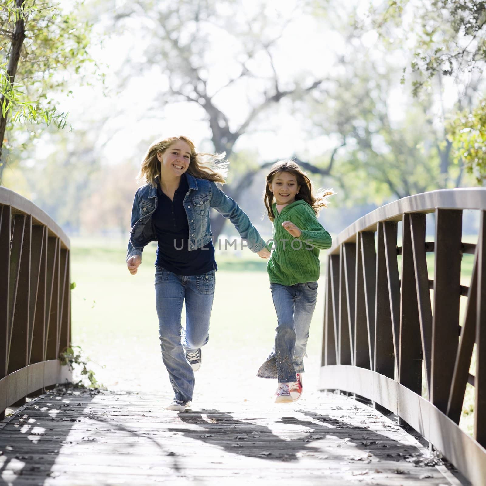 Two Girls Running Across a Bridge in a Park