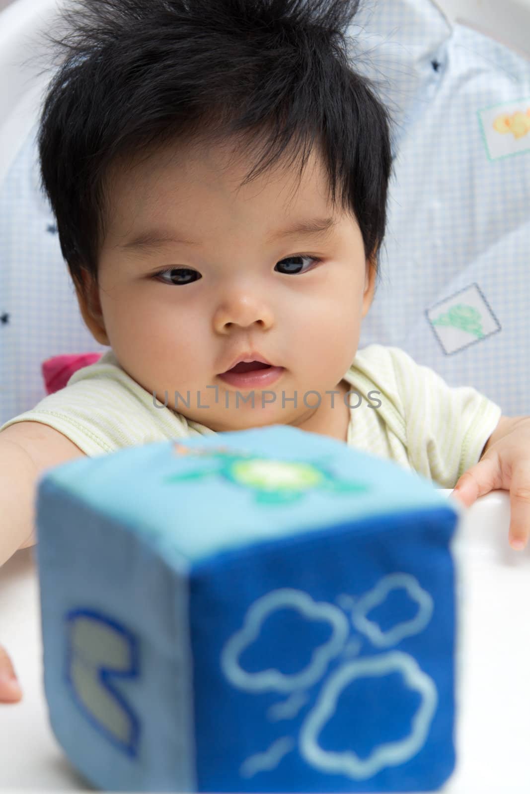 Little Asian baby girl on a high chair playing with a blue soft cube
