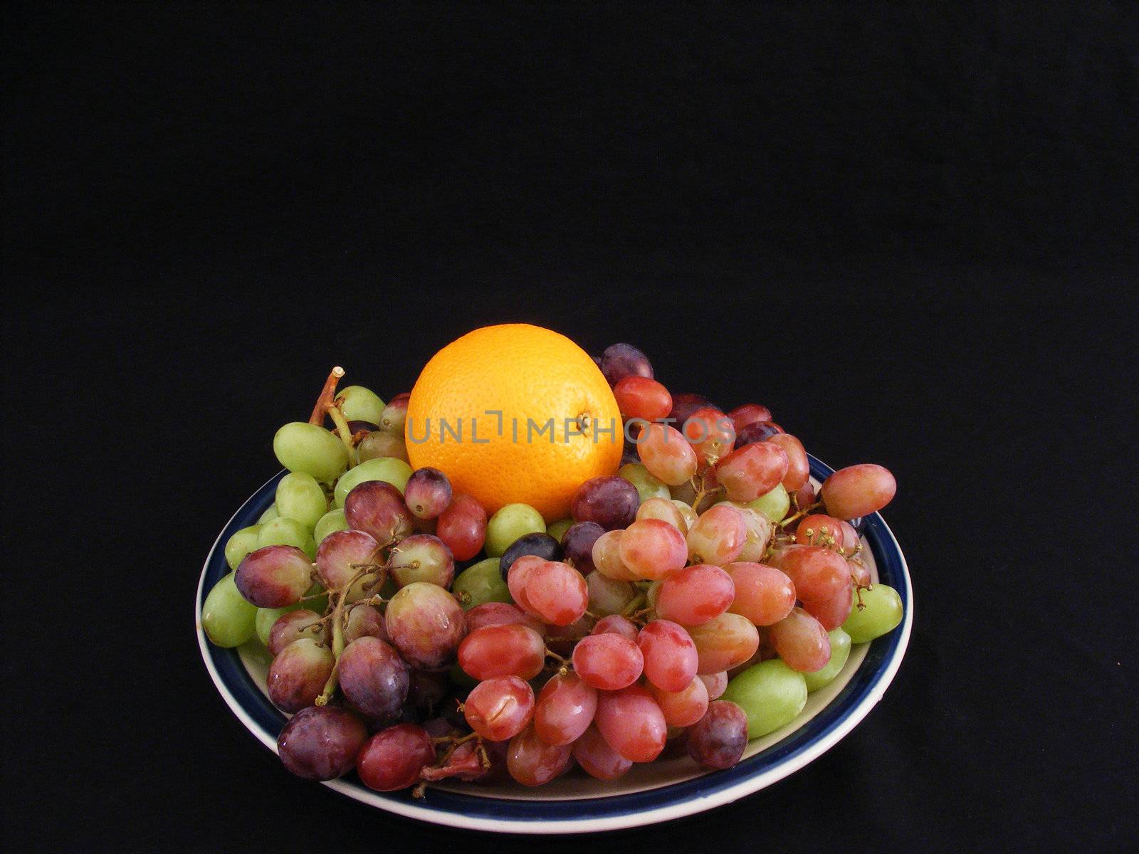 An orange nestled in a bed of grapes.