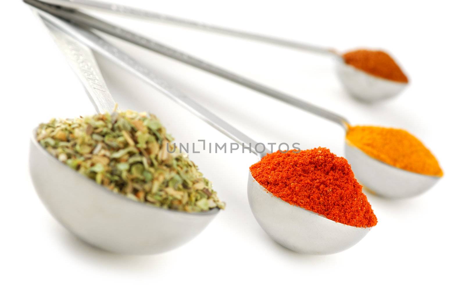 Assorted spices in metal measuring spoons on white background