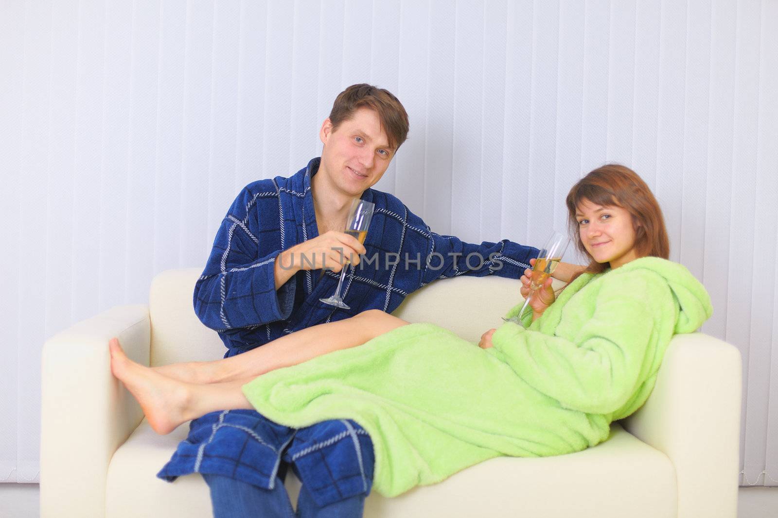 Young couple drinks sparkling wine on sofa in dressing gowns by pzaxe