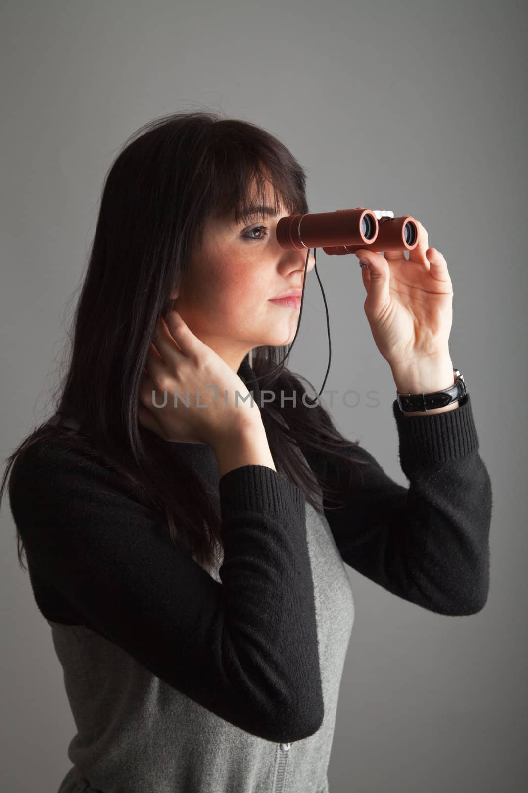 Front lit brunette woman looking via binoculars; gray background