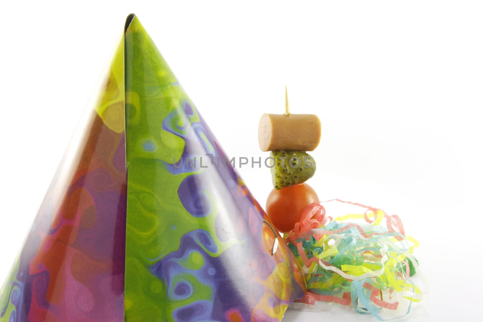 Multi coloured party hat with cocktail stick and streamers on a reflective white background