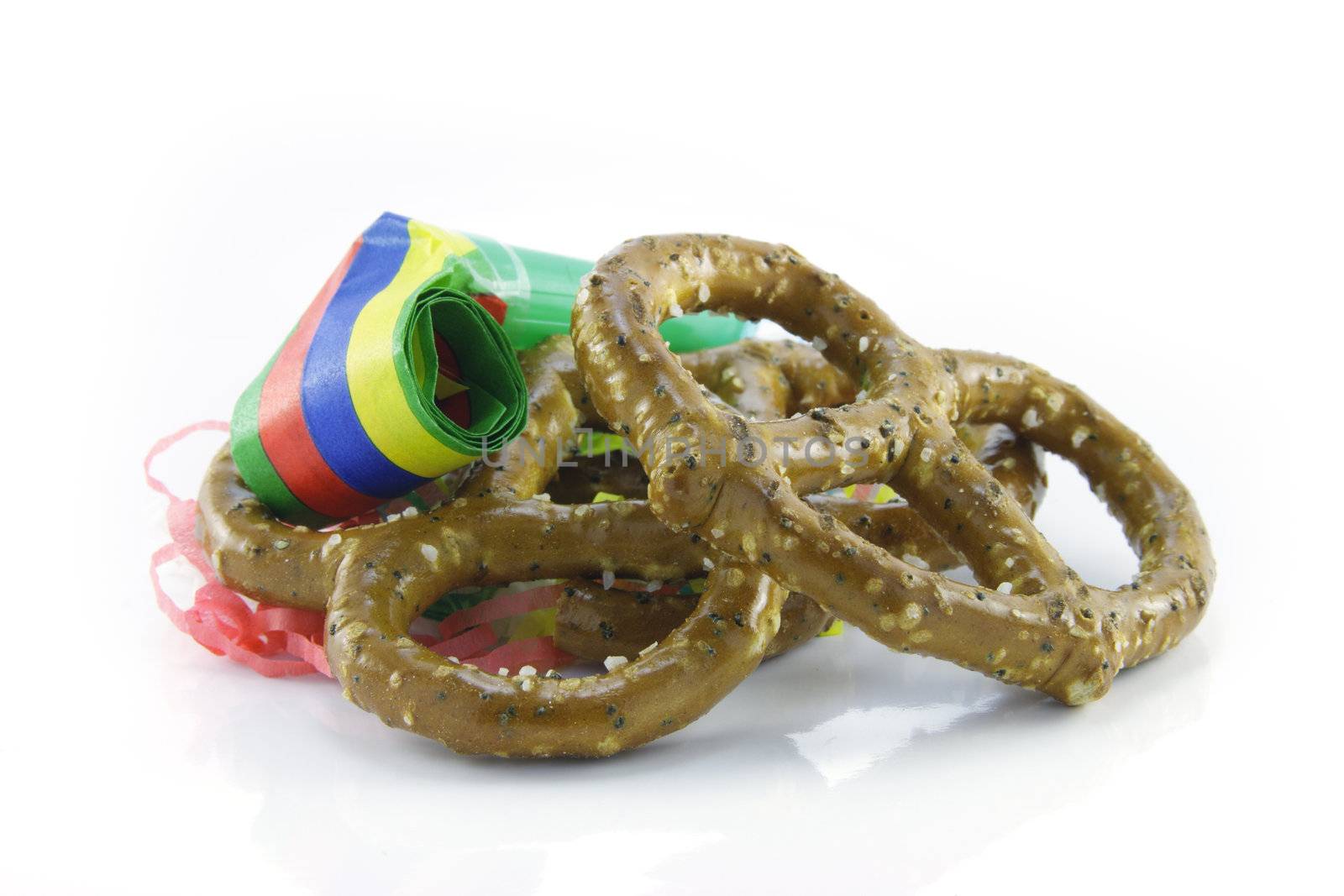Two salty baked pretzels with party streamers and party blower on a reflective white background