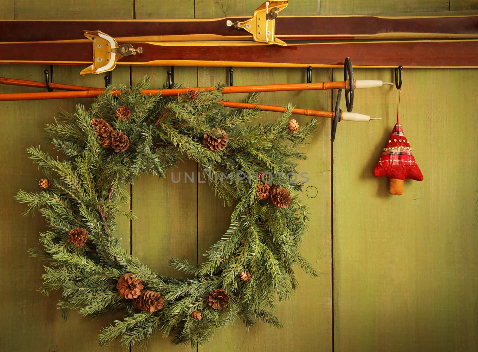 Old pair of skis hanging with wreath against green wood background