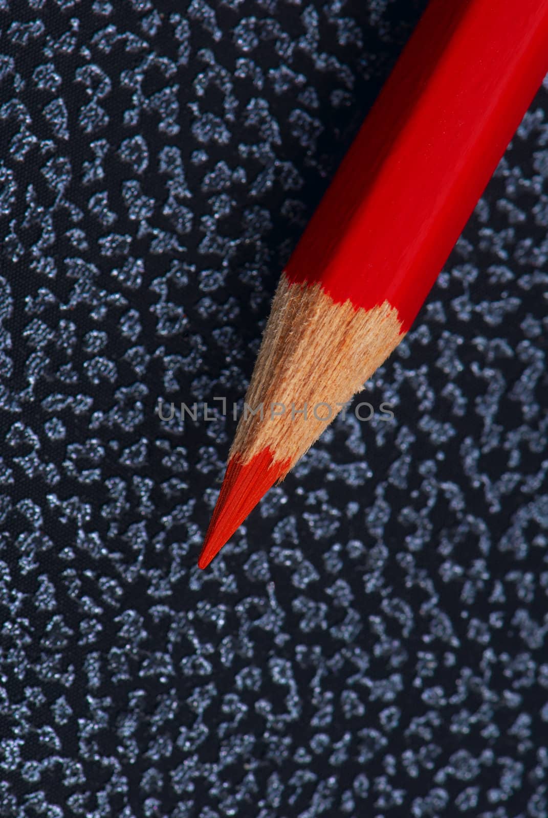 Red pencil on a notebook from an artificial leather. A close up