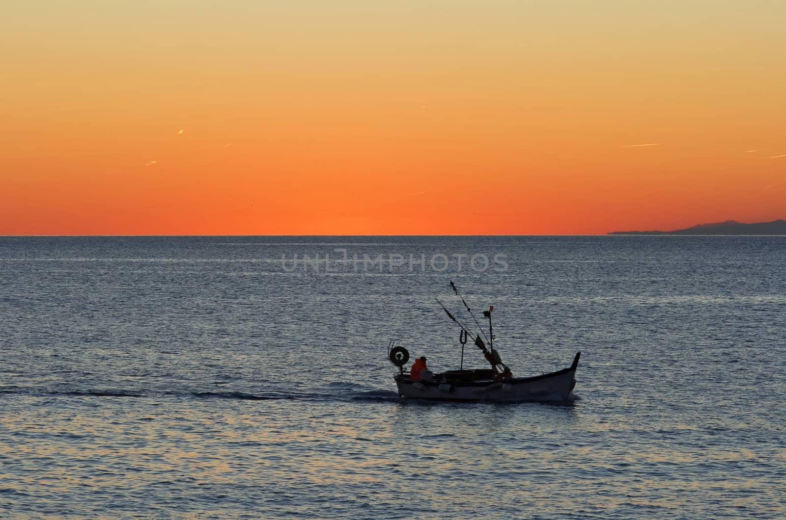 beautiful sunset in Mediterranean sea while a fishing boat returns to port