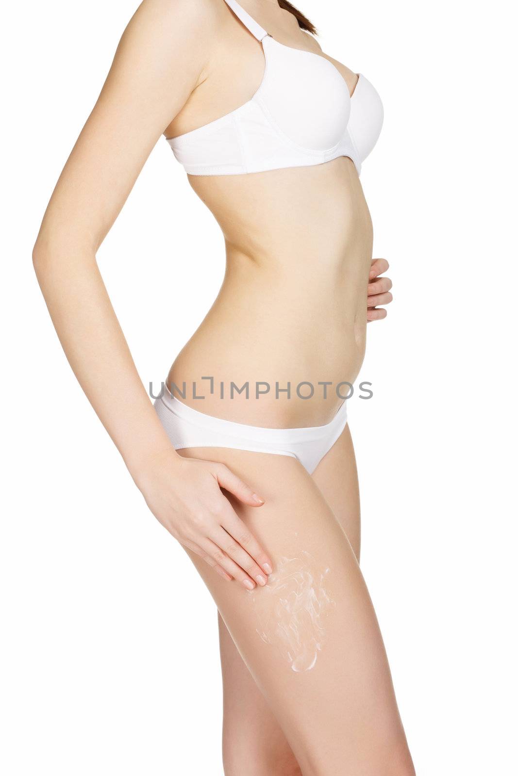 Slim woman applying moisturizer cream on her legs, isolated on white background
