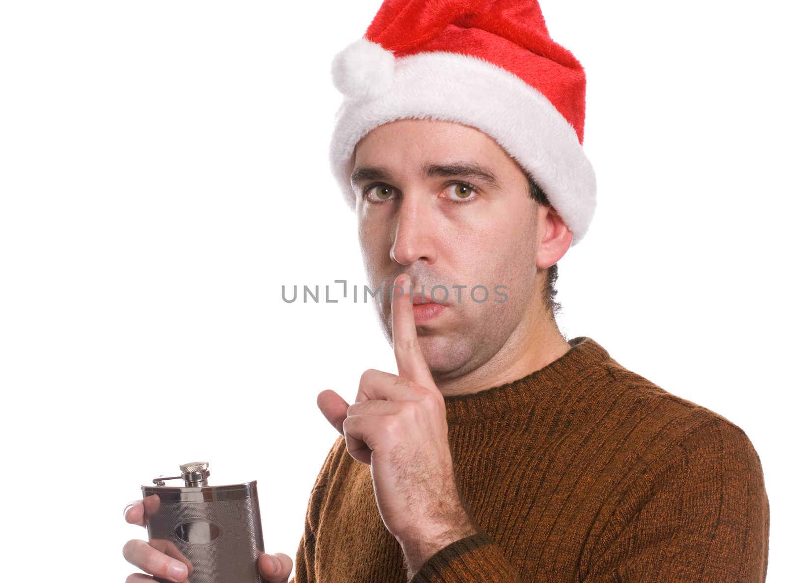 A young man wearing a santa hat is holding an alcohol flask and covering his lips with his finger, isolated against a white background