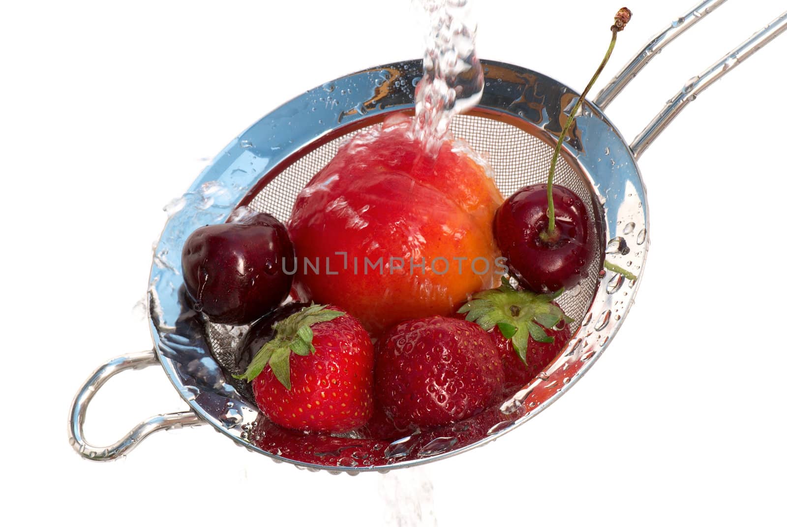 Ripe strawberry, cherry and peach in a colander under a jet of pure water.