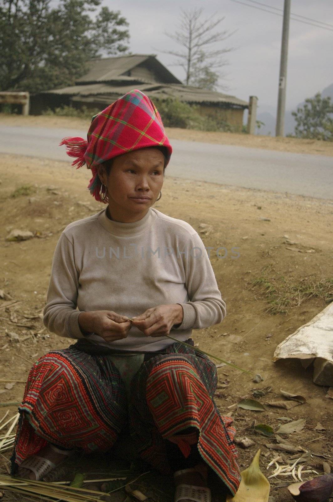 This woman from flowered Hmong  ethnic group of northern Vietnam is sitting at the roadside to make links to attach the flowers she sells banana