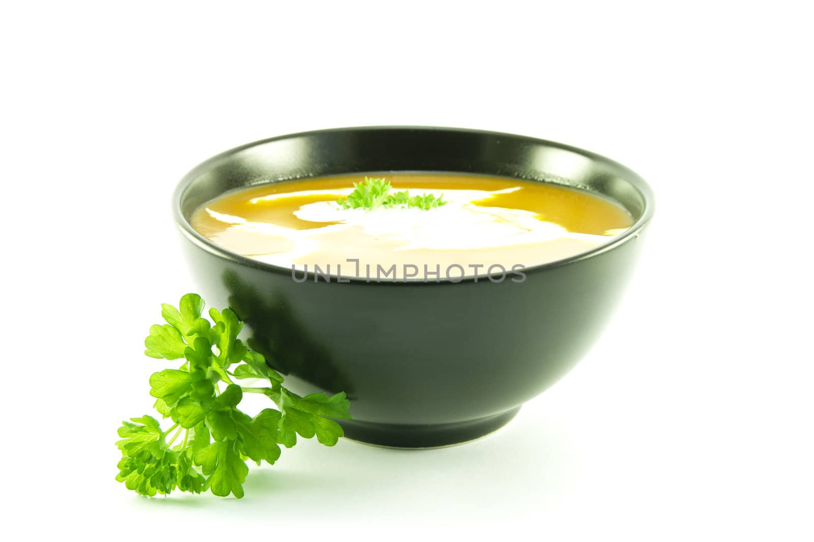 Rich red deliicious tomato soup in a small round black bowl with cream and a sprig of parsley on a white background