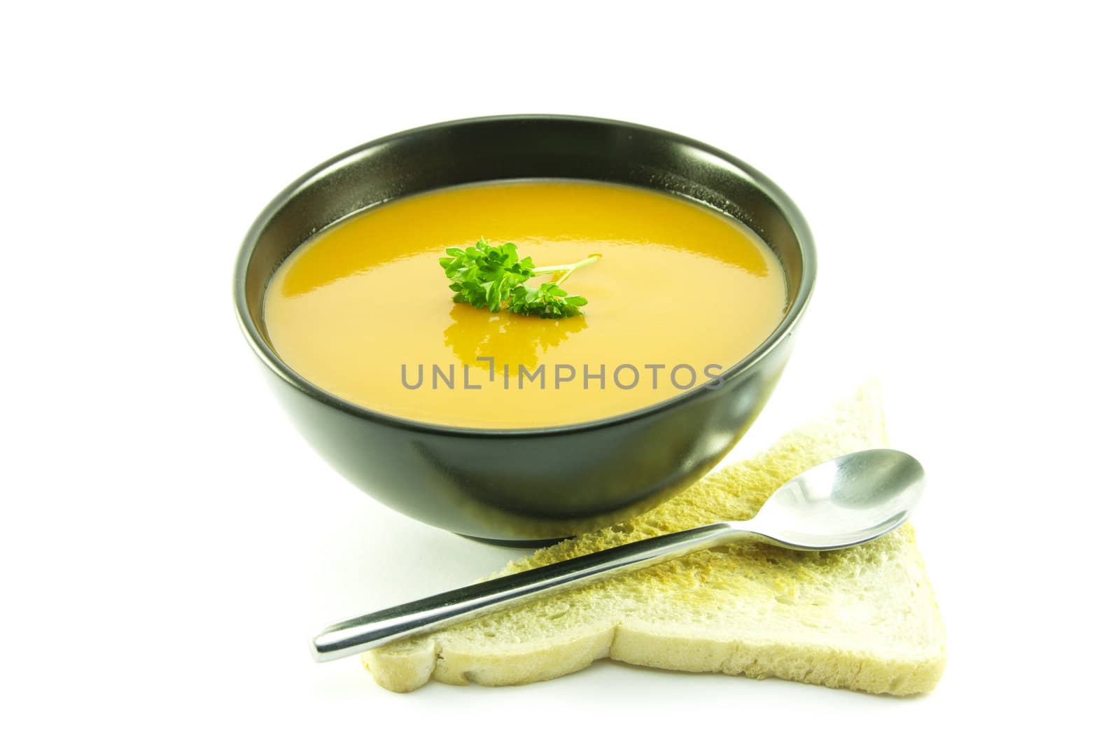 Rich red deliicious tomato soup in a small round black bowl with a sprig of parsley, toast and a spoon on a white background