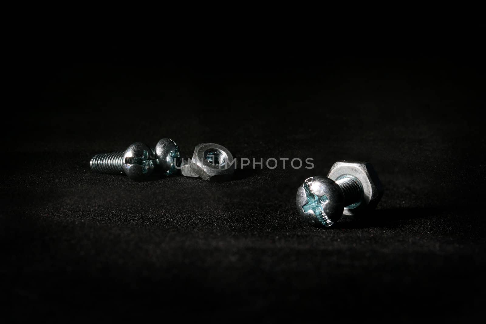 The connected bolt and nut in the foreground both two separately a bolt and two nuts on a black background.