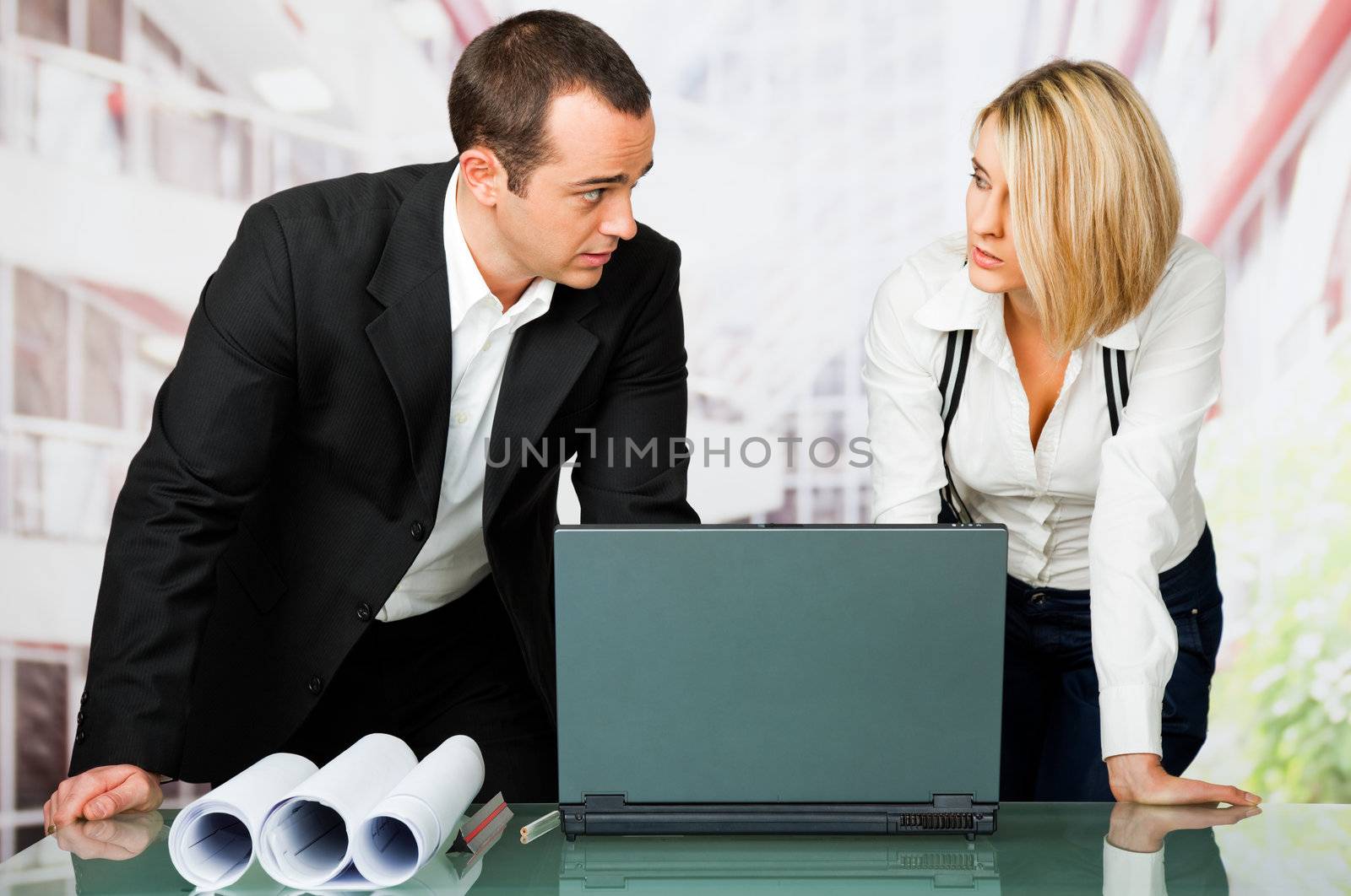 Male and female architects standing over laptop and blueprints, discussing