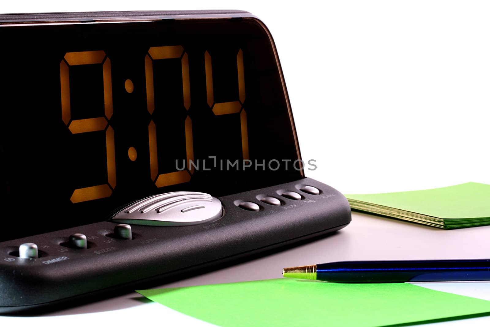 Electronic clock for office or the house, show time. In the foreground the handle and leaves of a paper for messages.