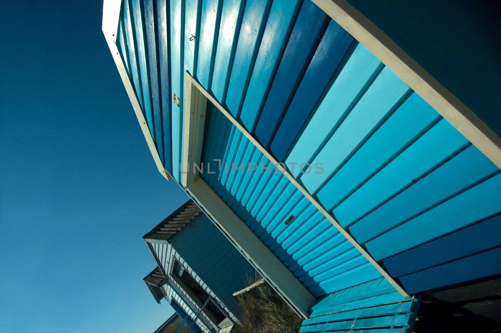 A Colourful Blue photo of a Row of Beach Huts on a Sunny Summers Day