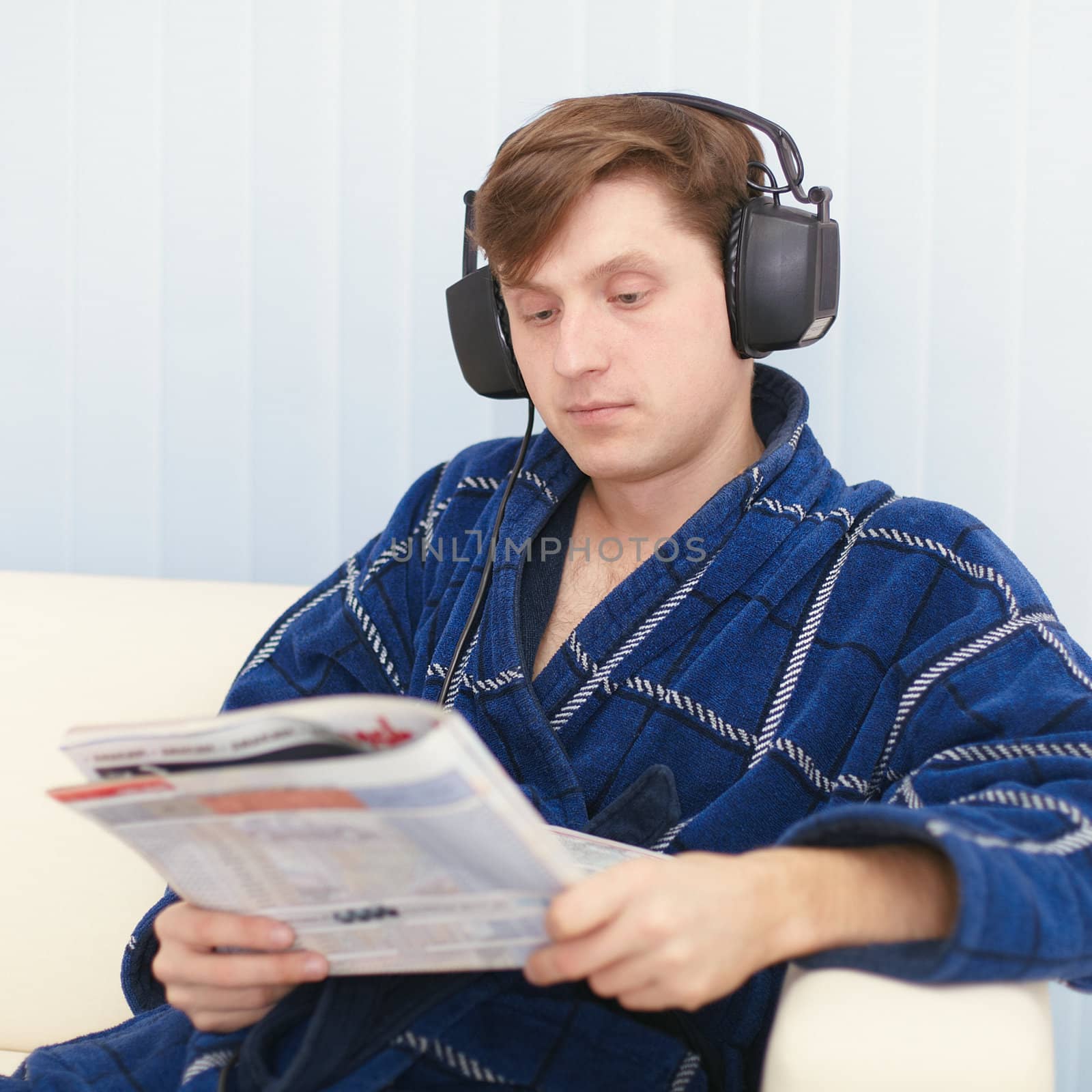 Man in big ear-phones on sofa reads newspaper by pzaxe